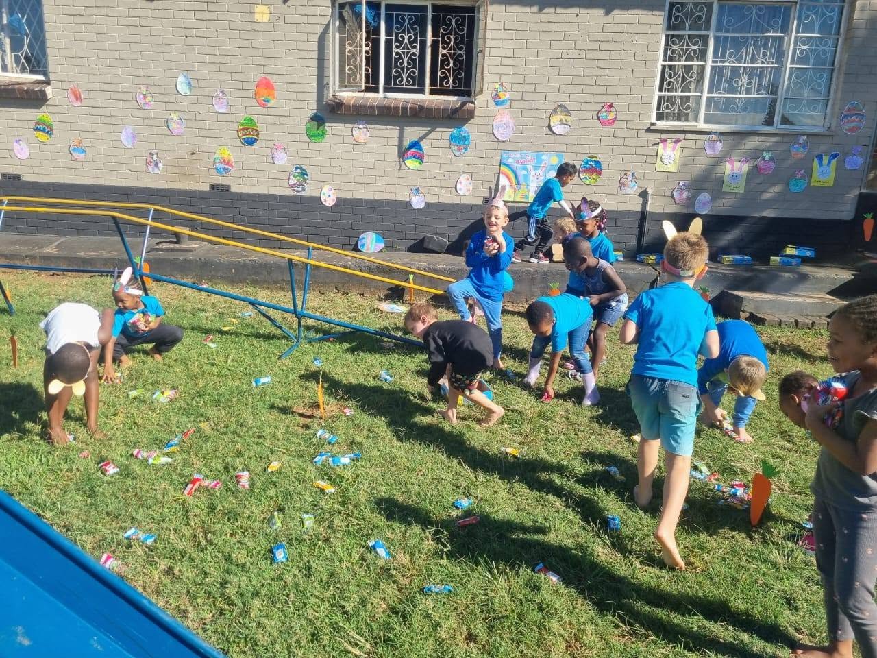 Children wearing bunny ears gathering Easter treats in the Emojis school garden
